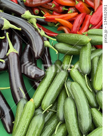 Fresh vegetables market display featuring cucumbers, eggplants, and red peppers on green surface Fresh vegetables market display featuring cucumbers, eggplants, and red peppers on green surface 134682061