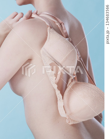Naked woman holds beige bra in hand Naked woman holds beige bra in hand 134683566