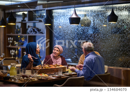 Muslim family shares iftar in a restaurant with Ramadan decorations and warm lighting during the holy month 134684070