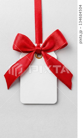 White gift tag with red ribbon hangs against a plain background ready for personalization and holiday use White gift tag with red ribbon hangs against a plain background ready for personalization and holiday use 134684504