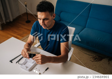 High-angle view of technician male assembling wi-fi module using tools at home office desk, focusing on intricate components and ensuring proper connection. Concept of desktop PC maintenance 134684901