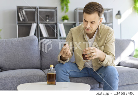 Man with alcohol addiction holding whiskey and cigarette at home, health risk 134685400