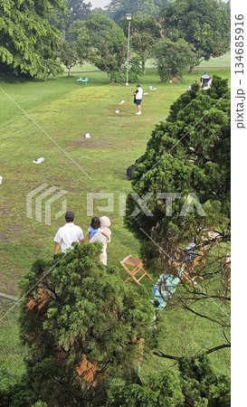 Golfers gather on a grassy field with chairs, gear, and a cart nearby, enjoying a relaxed outdoor setting surrounded by trees 134685916