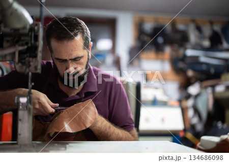 Skilled craftsman in a leather workshop stitching and repairing a shoe with focus 134686098