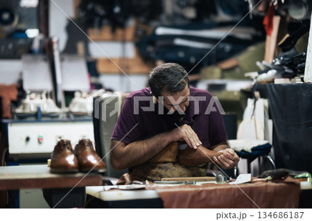 Cobbler at work polishing a leather boot in a busy workshop, focusing on craftsmanship 134686187