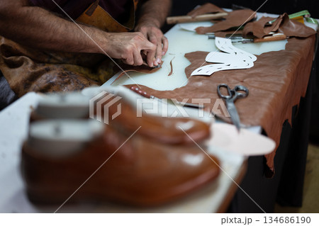 Leather craftsman at work shaping leather with tools and patterns on a workshop table Leather craftsman at work shaping leather with tools and patterns on a workshop table 134686190