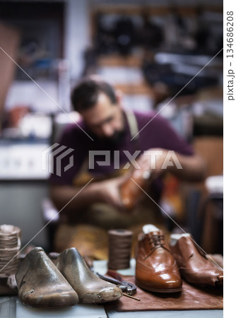Cobbler at work in a leather shoe workshop shaping brown and metallic shoes with tools 134686208