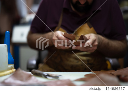Leather craftsman at work shaping pieces into wallets in a busy workshop 134686237