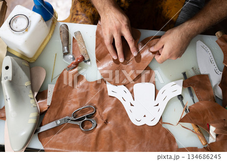 Leather workshop scene of hands crafting a decorative mask with tools and templates Leather workshop scene of hands crafting a decorative mask with tools and templates 134686245