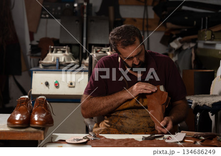 Shoemaker crafts leather shoes in a busy workshop with tools and leather pieces 134686249