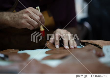 Leather craft in progress: close-up of hands shaping leather pieces with a tool 134686250