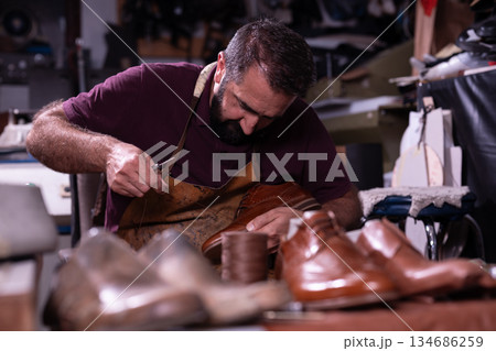 Skilled shoemaker crafts leather shoe in workshop with careful stitching Skilled shoemaker crafts leather shoe in workshop with careful stitching 134686259