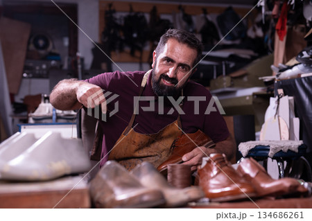 Cobbler at work in a leather workshop crafting brown dress shoes with focused skill and craft 134686261