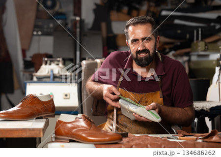 Cobbler at work in a leather workshop, crafting and measuring high-quality shoes Cobbler at work in a leather workshop, crafting and measuring high-quality shoes 134686262
