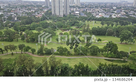 A glowing golf course with sand bunkers and floodlights stretches beneath ornate towers and a vivid sunset, blending sport, architecture, and nature in a dramatic dusk cityscape in Jakarta 134686264