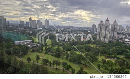 A glowing golf course with sand bunkers and floodlights stretches beneath ornate towers and a vivid sunset, blending sport, architecture, and nature in a dramatic dusk cityscape in Jakarta 134686265