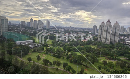 A glowing golf course with sand bunkers and floodlights stretches beneath ornate towers and a vivid sunset, blending sport, architecture, and nature in a dramatic dusk cityscape in Jakarta 134686266
