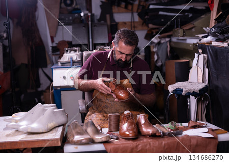 Shoemaker at work crafting leather shoes in a busy workshop with tools and scraps today Shoemaker at work crafting leather shoes in a busy workshop with tools and scraps today 134686270