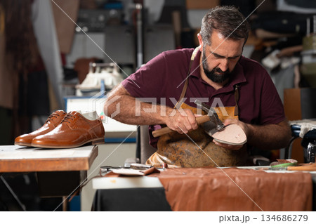 Cobbler at work repairing a leather shoe in a busy workshop 134686279