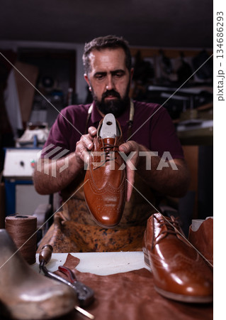 Cobbler presents a polished brown leather oxford shoe in a busy workshop with tools Cobbler presents a polished brown leather oxford shoe in a busy workshop with tools 134686293