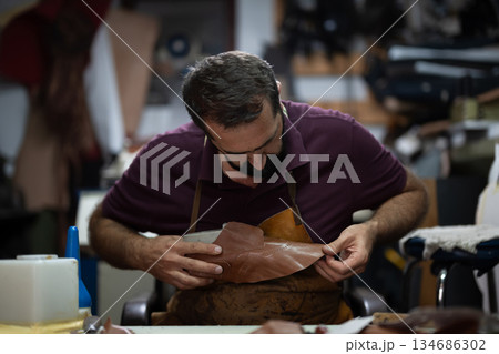 Cobbler shaping leather shoe in a busy workshop, a focused artisan at work on intricate stitching Cobbler shaping leather shoe in a busy workshop, a focused artisan at work on intricate stitching 134686302