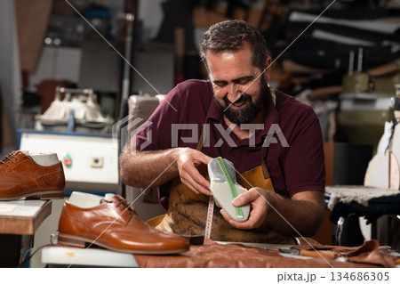 Master craftsman at work polishing and measuring a leather shoe in a busy workshop today 134686305
