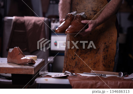 Shoemaker holds polished brown leather shoes in a workshop during a crafting session Shoemaker holds polished brown leather shoes in a workshop during a crafting session 134686313