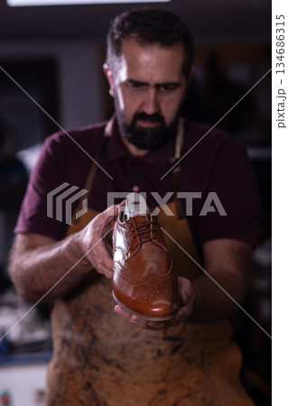 Shoemaker presents polished brown leather dress shoe in workshop, showcasing craftsmanship and traditional shoemaking details 134686315