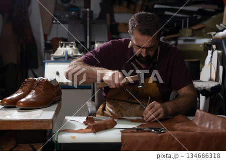 Shoemaker at work repairing leather shoes with hammer and awl in a busy workshop 134686318