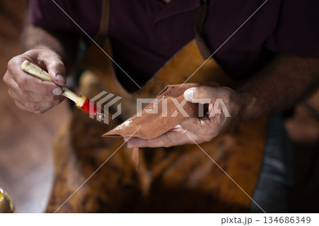 Artisan hand paints leather piece with brush, crafting detailed leatherwork by hand 134686349