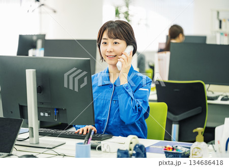 オフィスで電話対応する作業服を着た若い女性 オフィスで電話対応する作業服を着た若い女性 134686418