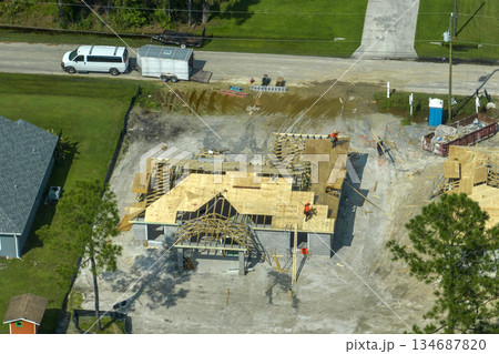 Professional builders working on roof construction of unfinished suburban home with wooden frame structure in Florida rural area. Concept of housing development in America 134687820