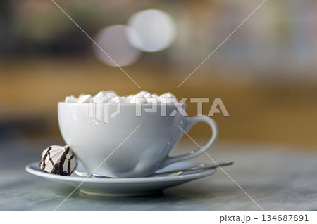 Mug of coffee with marshmallows on porcelain plate on blurred colorful interior bokeh background. 134687891