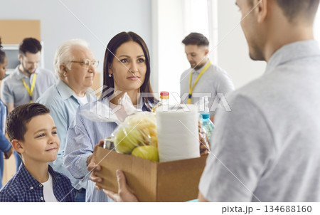 A young mother with a child takes a box of groceries from a volunteer 134688160