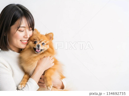 ポメラニアンを抱っこして笑顔の女性　愛犬との幸せな暮らし　ペットライフ　明るい室内　ライフスタイル 134692735