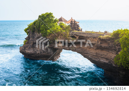Batu Bolong Temple iconic Hindu shrine on rocky arch along Bali coast attracts travelers with ocean waves, sacred Balinese architecture, Batu Bolong dramatic cliffs, spiritual atmosphere in daylight Batu Bolong Temple iconic Hindu shrine on rocky arch along Bali coast attracts travelers with ocean waves, sacred Balinese architecture, Batu Bolong dramatic cliffs, spiritual atmosphere in daylight 134692814
