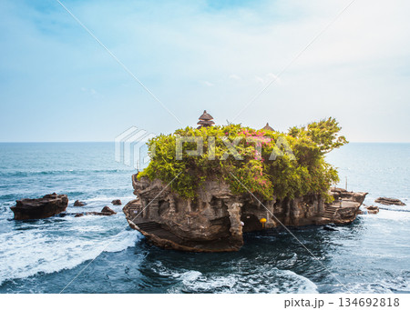 Tanah Lot temple Bali sea rock iconic landmark, ancient Hindu shrine on ocean cliff amid crashing waves lush greenery blue sky, exotic tropical Indonesian paradise coastal landscape travel destination 134692818