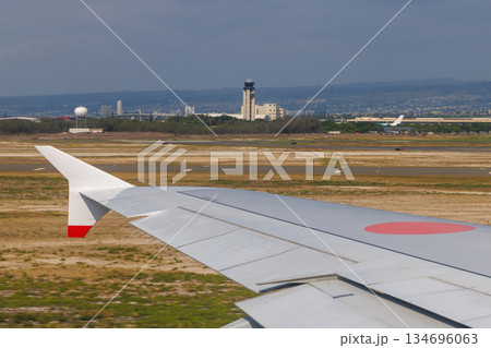 ホノルル空港を離陸するジェット機の翼、遠方に見える管制塔 ホノルル空港を離陸するジェット機の翼、遠方に見える管制塔 134696063