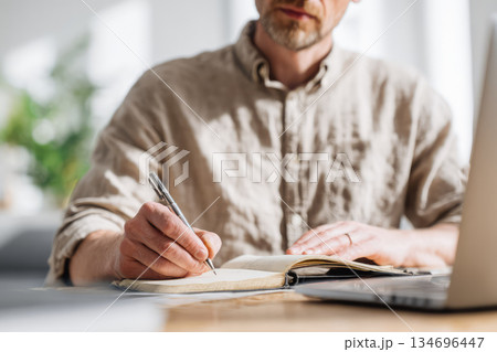 Writing in five minute journal, man sits at desk with pen in hand, focused and thoughtful, natural light streaming in through window, calm and peaceful atmosphere 134696447
