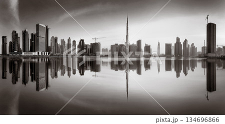 Monochrome city skyline with tall skyscrapers reflecting on calm water under a cloudy sky, Dubai Marina bay UAE Monochrome city skyline with tall skyscrapers reflecting on calm water under a cloudy sky, Dubai Marina bay UAE 134696866
