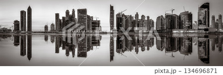 Monochrome city skyline with tall skyscrapers reflecting on calm water under a cloudy sky, Dubai Marina bay UAE Monochrome city skyline with tall skyscrapers reflecting on calm water under a cloudy sky, Dubai Marina bay UAE 134696871