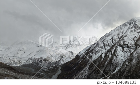 Snowy mountain landscape with dramatic clouds and winding river below 134698133