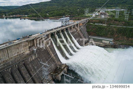 Aerial view of concrete dam releasing water into river on cloudy day. Water discharge at hydroelectric power plant. Aerial view of concrete dam releasing water into river on cloudy day. Water discharge at hydroelectric power plant. 134699854