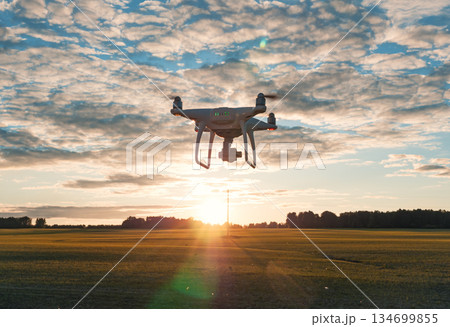 A drone soars through the sky above vast open fields as the sun sets on the horizon A drone soars through the sky above vast open fields as the sun sets on the horizon 134699855