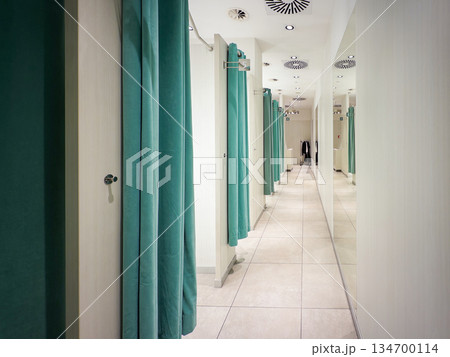 Modern retail changing room hallway featuring teal privacy curtains, a reflective mirrored wall, and ceiling ventilation, ready for customer trying clothes 134700114