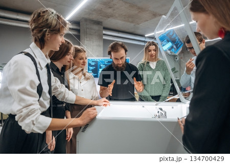 Explaining how the device works. People are in the office by the 3d printer 134700429
