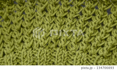 Knitting pattern using thick green yarn. Needles, thread, and green fabric 134700893