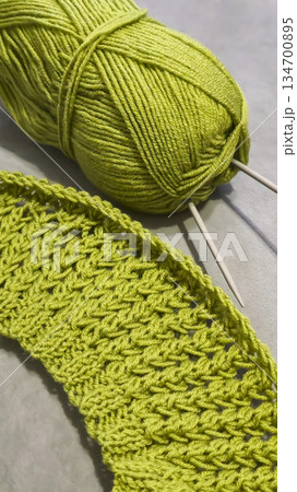 Knitting pattern using thick green yarn. Needles, thread, and green fabric 134700895