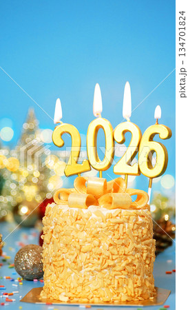 Happy New Year 2026, cute cake with golden ribbon with candle number 2026 for new year celebrate party was lit. decorated with Christmas ornament at blue background, vertical 134701824