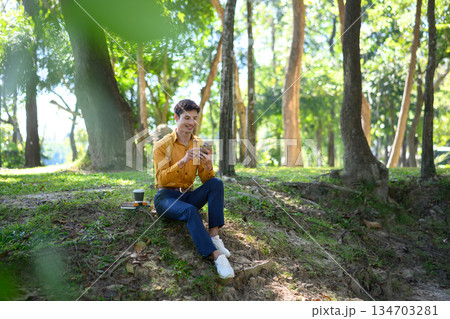 A man from an office sits on the grass in a green park using his phone in a relaxed mood A man from an office sits on the grass in a green park using his phone in a relaxed mood 134703281